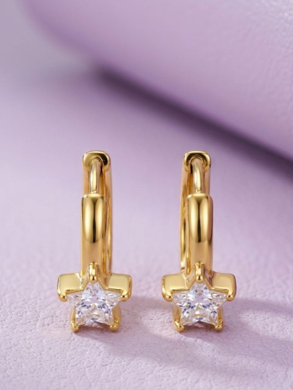 Close-up of two gold-plated star cubic zirconia hoop earrings against a soft lavender background