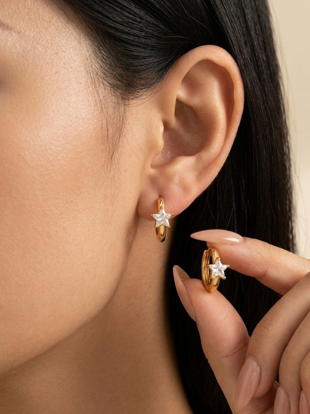 Woman wearing one gold star hoop earring while holding the second between manicured fingers