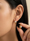 Woman wearing one gold star hoop earring while holding the second between manicured fingers