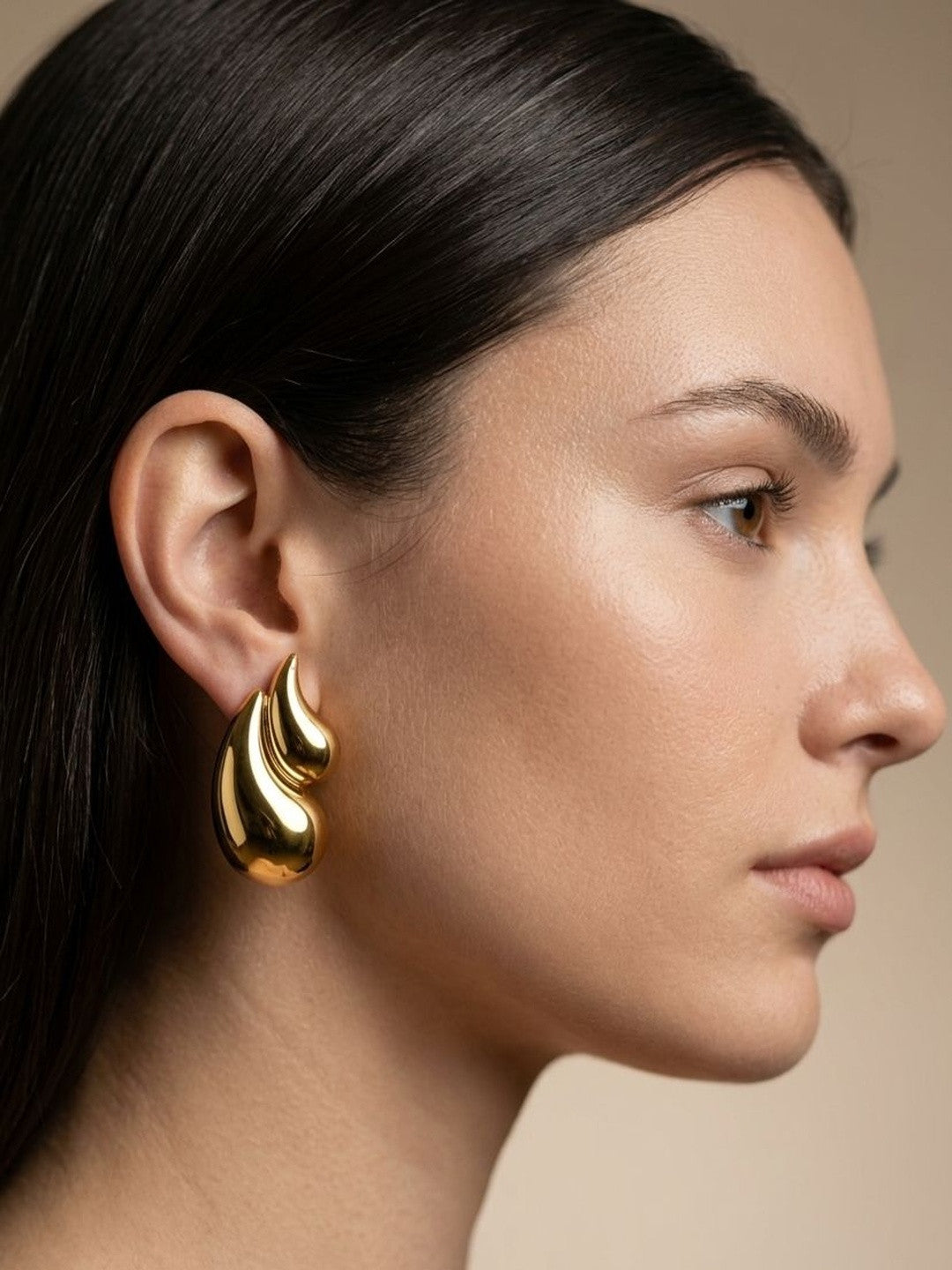 Side profile of a woman with dark hair wearing a gold-toned chunky flame drop stud earring on her left ear