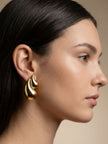 Side profile of a woman with dark hair wearing a gold-toned chunky flame drop stud earring on her left ear