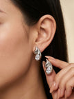 Woman wearing and holding silver crystal wing stud earrings, showing front and back view