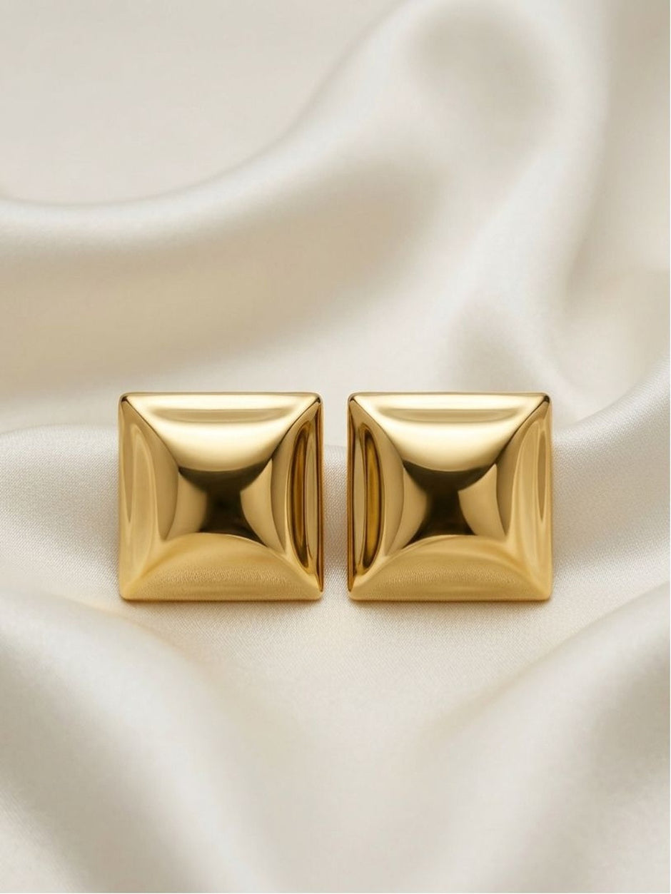 Pair of gold-plated square pyramid stud earrings on white satin fabric