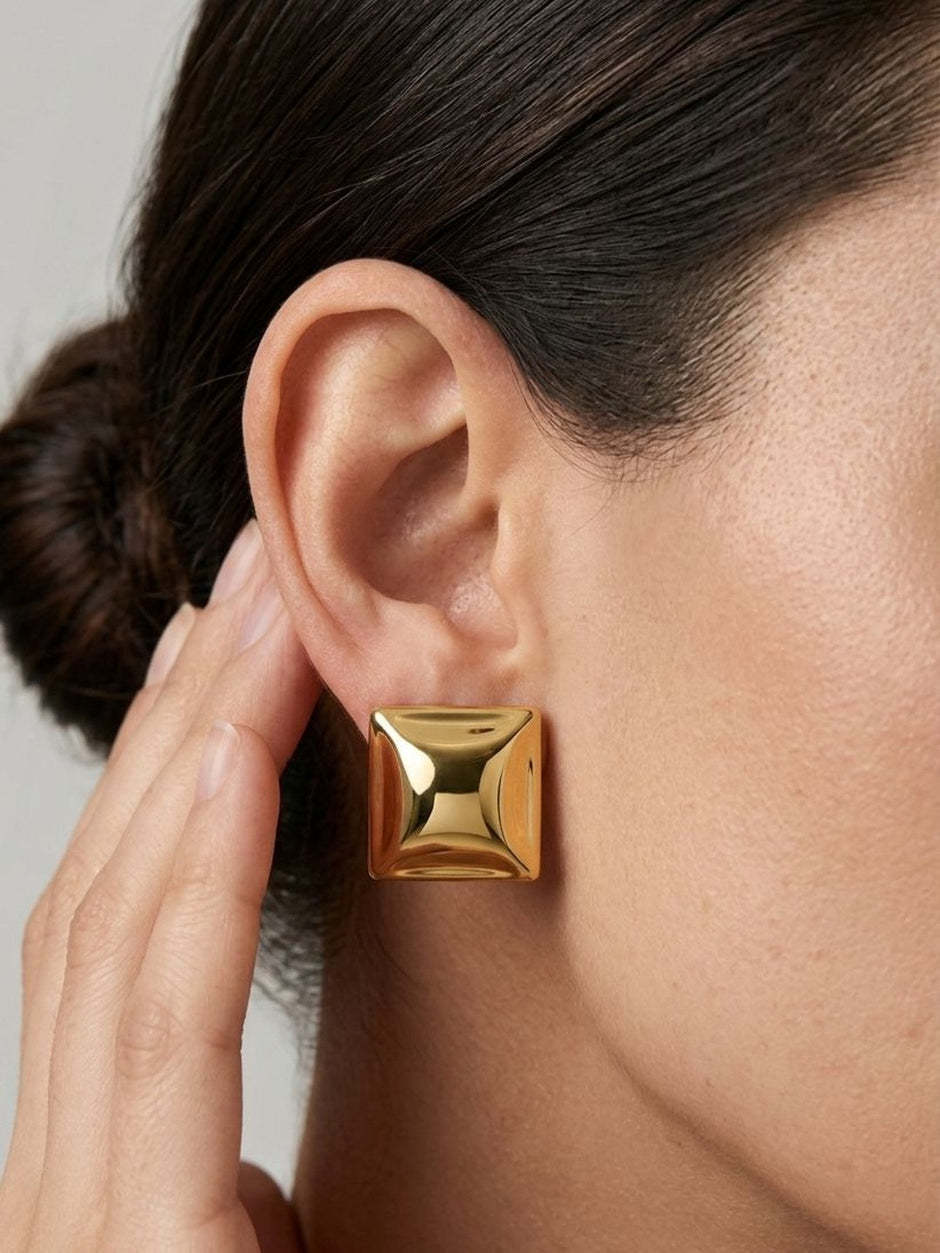 Close-up of gold pyramid square stud earring worn on a woman's ear