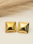 Pair of gold-plated square pyramid studs on white surface with dried grass backdrop