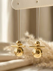 Two gold-toned ball and bar drop earrings hanging from a cream jewellery display card with pampas grass in background