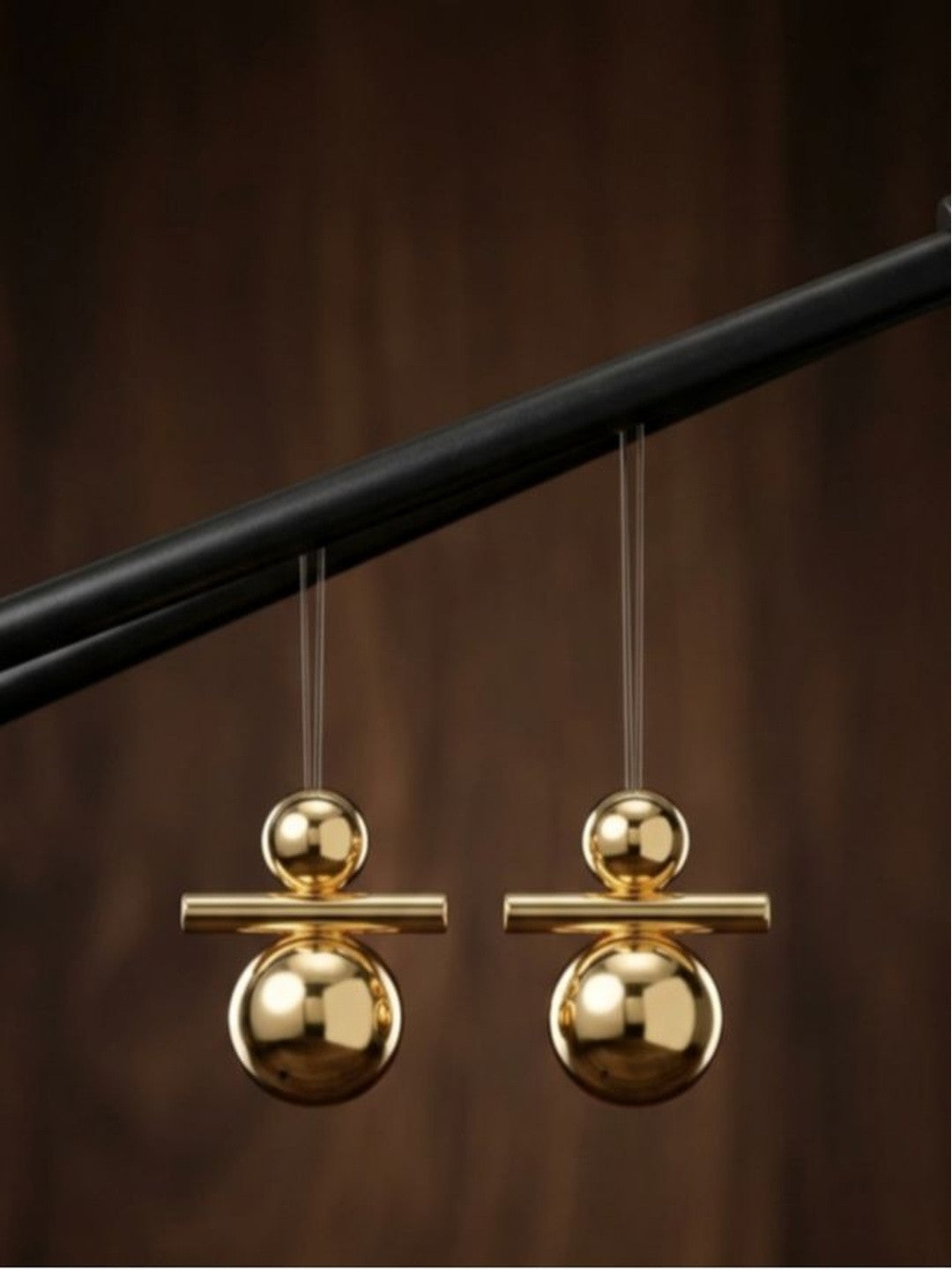 Pair of shiny gold geometric ball and bar drop earrings suspended on transparent threads against a dark wood background