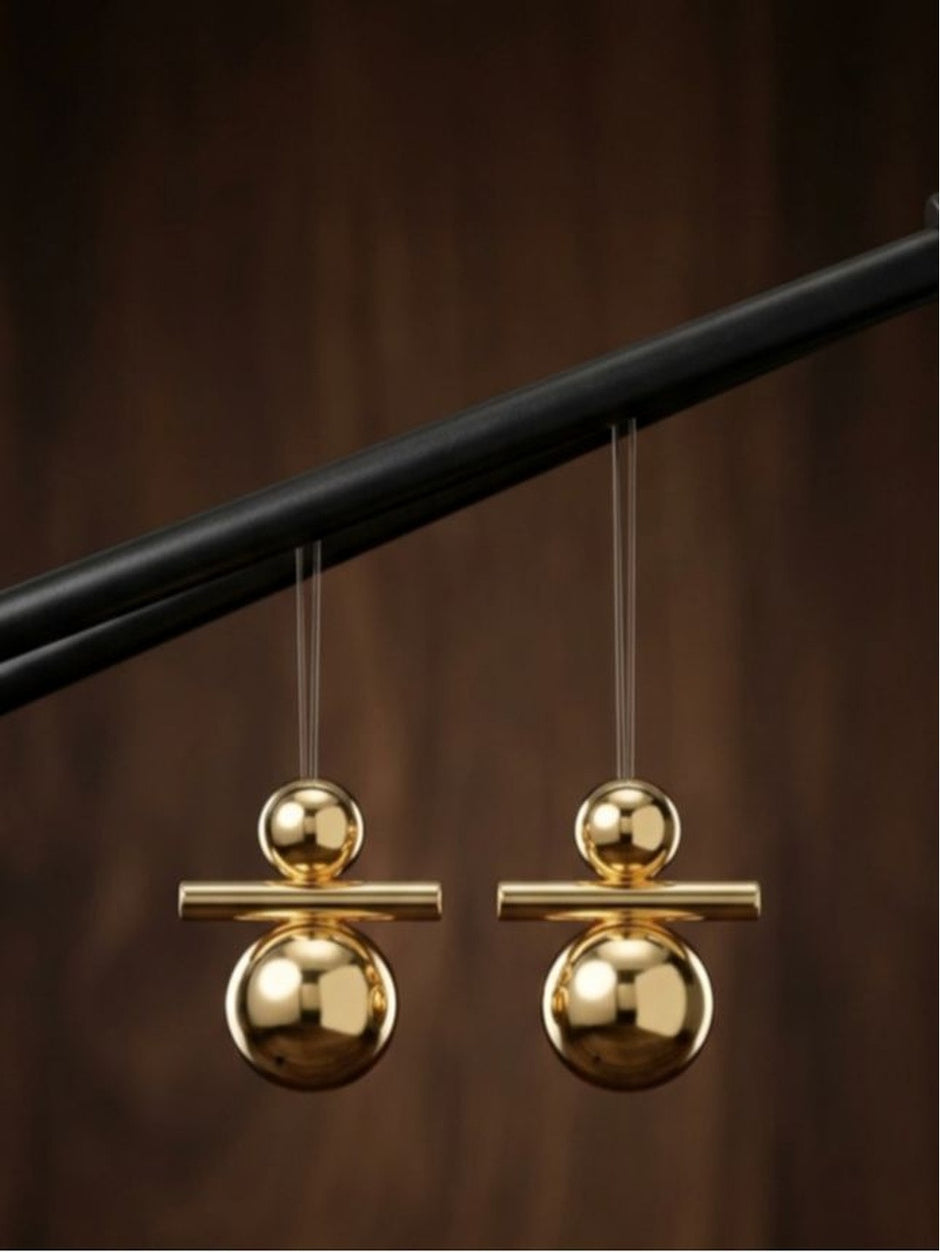 Pair of shiny gold geometric ball and bar drop earrings suspended on transparent threads against a dark wood background