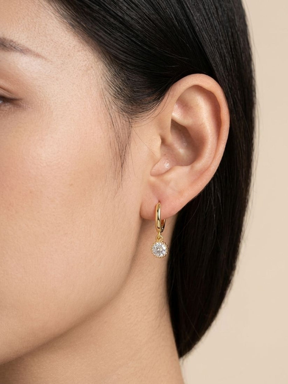 Gold hoop earring with crystal charm worn on a model's ear, side profile view