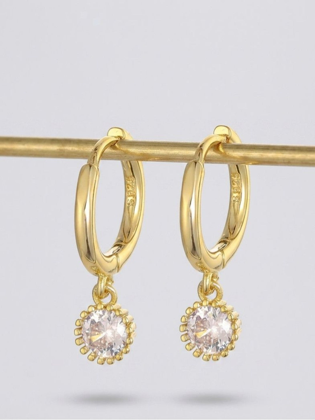 Two gold-plated crystal charm hoop earrings hanging from a brass display rod