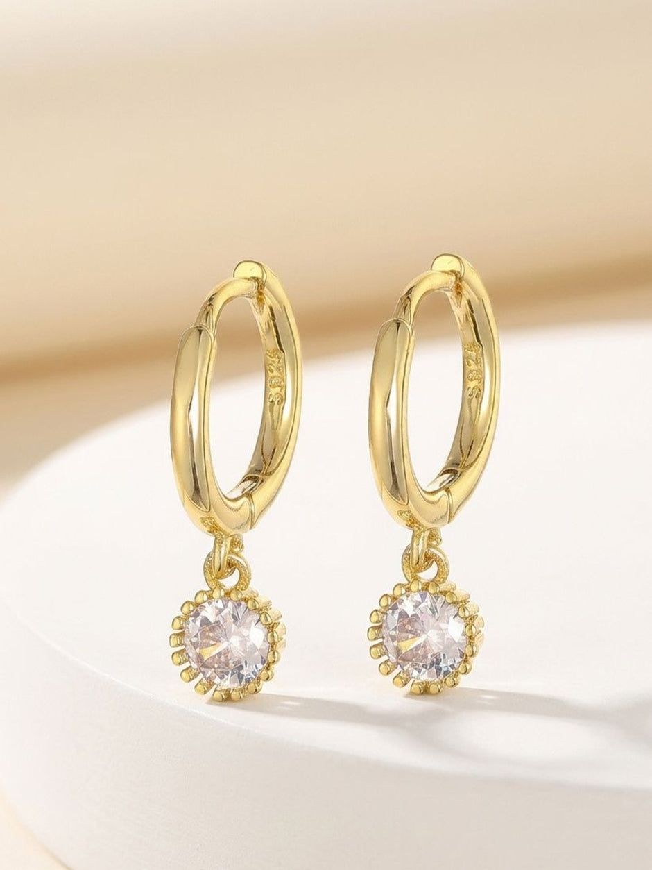 Gold hoop earrings with beaded crystal pendants resting on a white ceramic surface