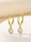 Gold hoop earrings with beaded crystal pendants resting on a white ceramic surface
