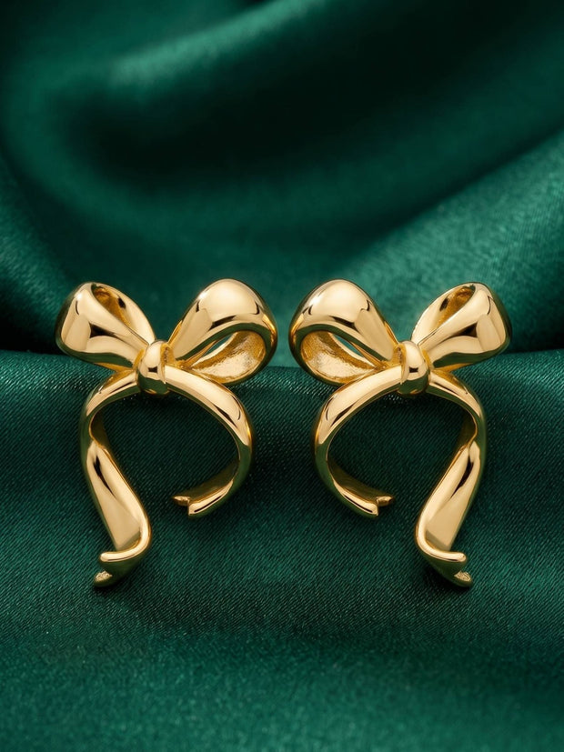 Pair of gold-plated bow stud earrings displayed on deep green satin fabric