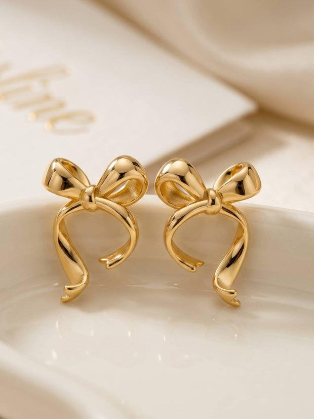 Two gold bow stud earrings resting on a white ceramic jewellery dish