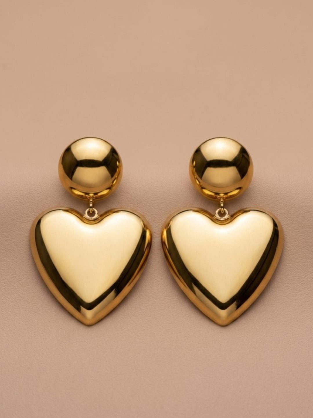 Pair of gold-plated puffy heart drop earrings laid flat on a beige surface