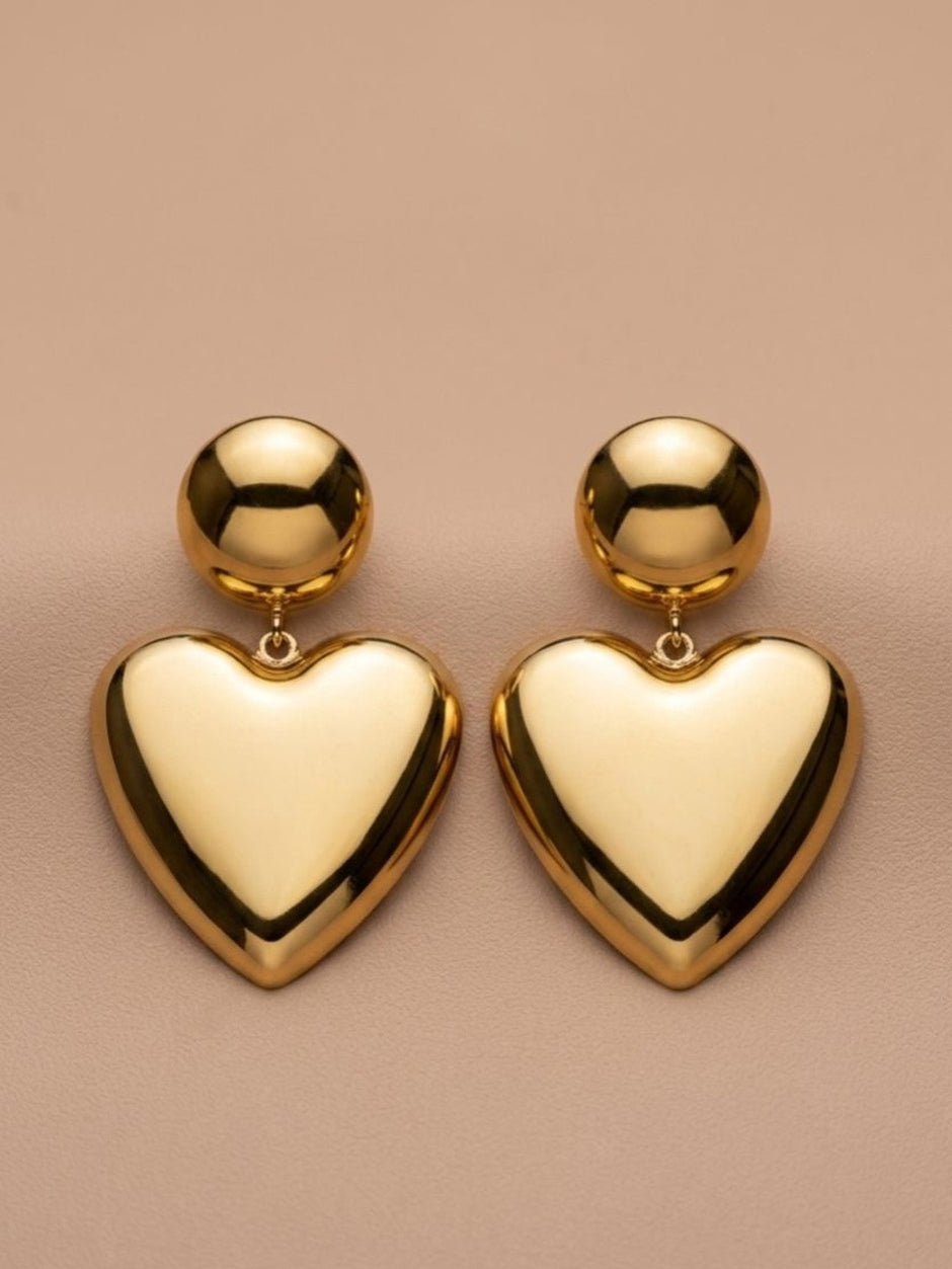 Pair of gold-plated puffy heart drop earrings laid flat on a beige surface