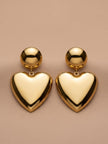 Pair of gold-plated puffy heart drop earrings laid flat on a beige surface