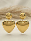 Gold heart drop earrings suspended on a display stand against a neutral linen background