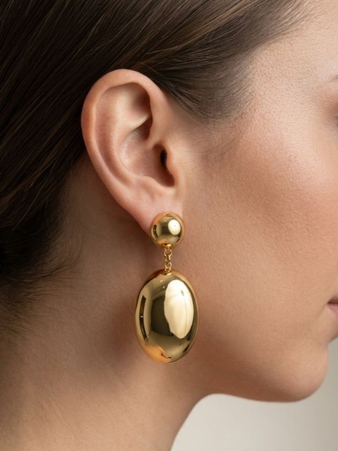 Close-up side profile of gold oval drop earring worn on a woman's ear