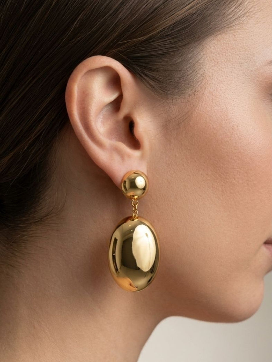 Close-up side profile of gold oval drop earring worn on a woman's ear