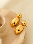Two gold-plated oval drop earrings laid flat on a cream ceramic dish from above
