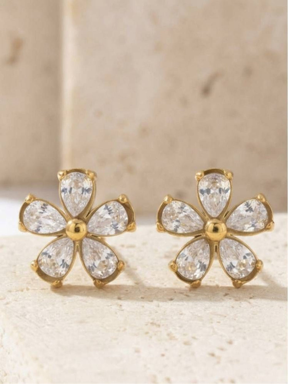 Gold-plated cubic zirconia floral stud earrings displayed on a beige stone surface