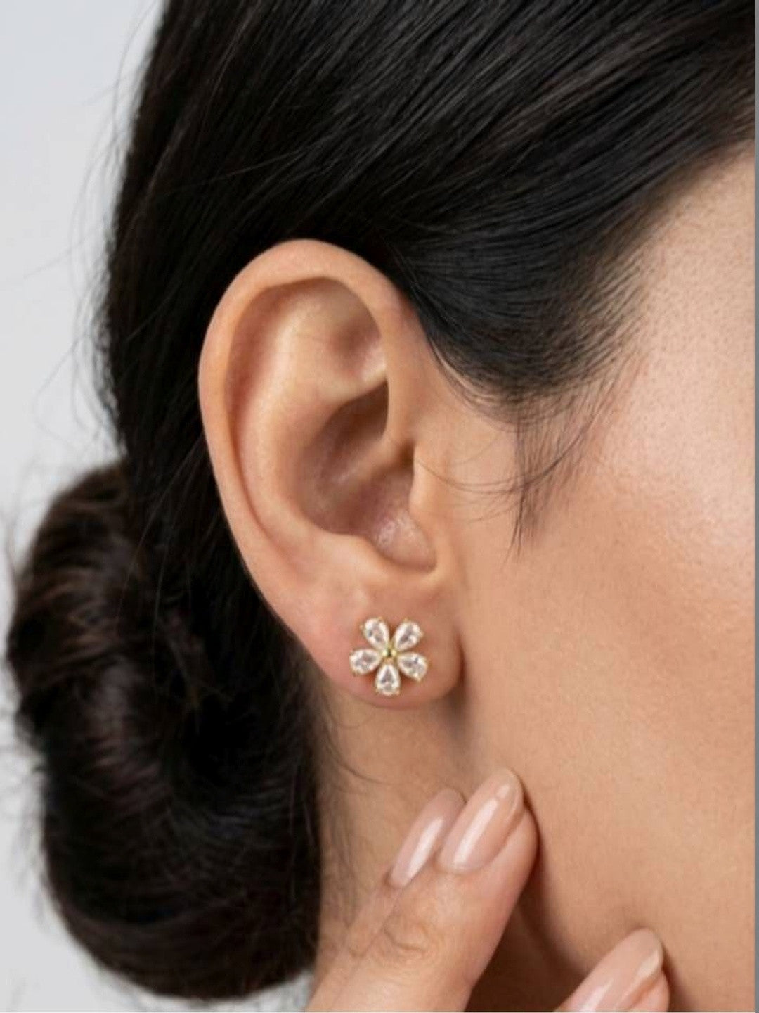 Woman wearing gold-plated cubic zirconia flower stud earring on her earlobe