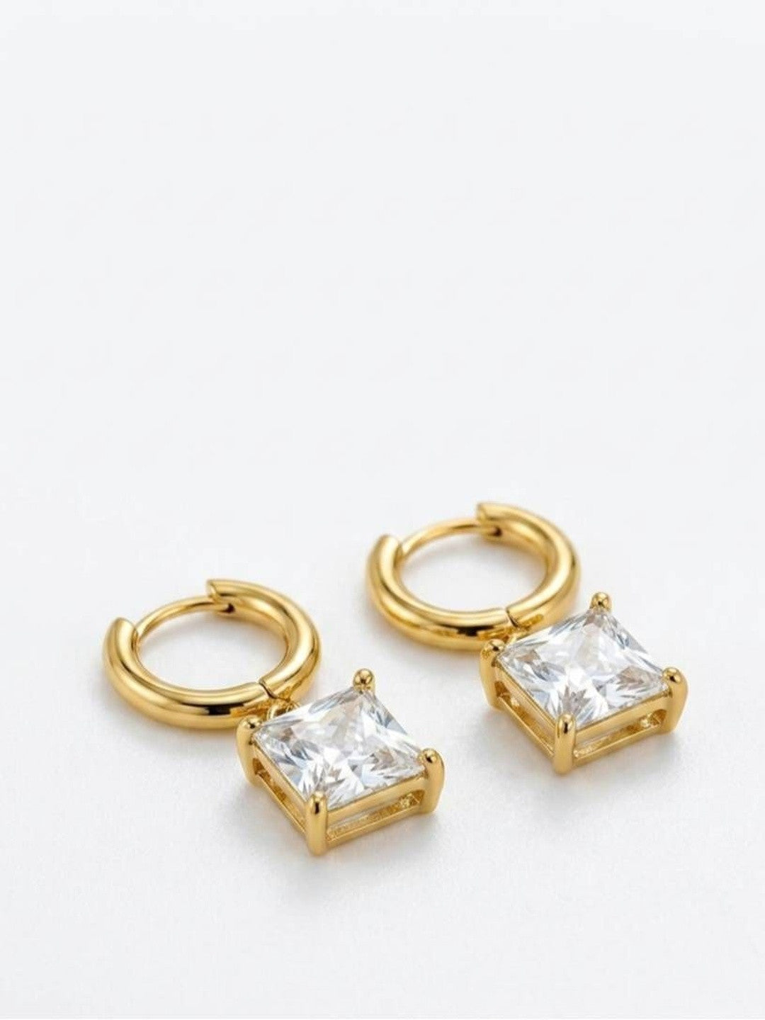 Pair of gold-plated huggie hoop earrings with square cubic zirconia charm pendants on white background