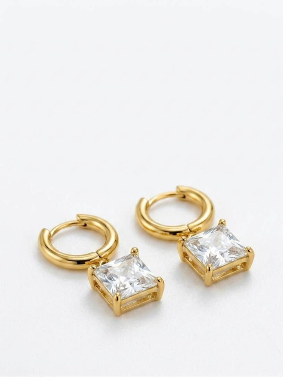 Pair of gold-plated huggie hoop earrings with square cubic zirconia charm pendants on white background