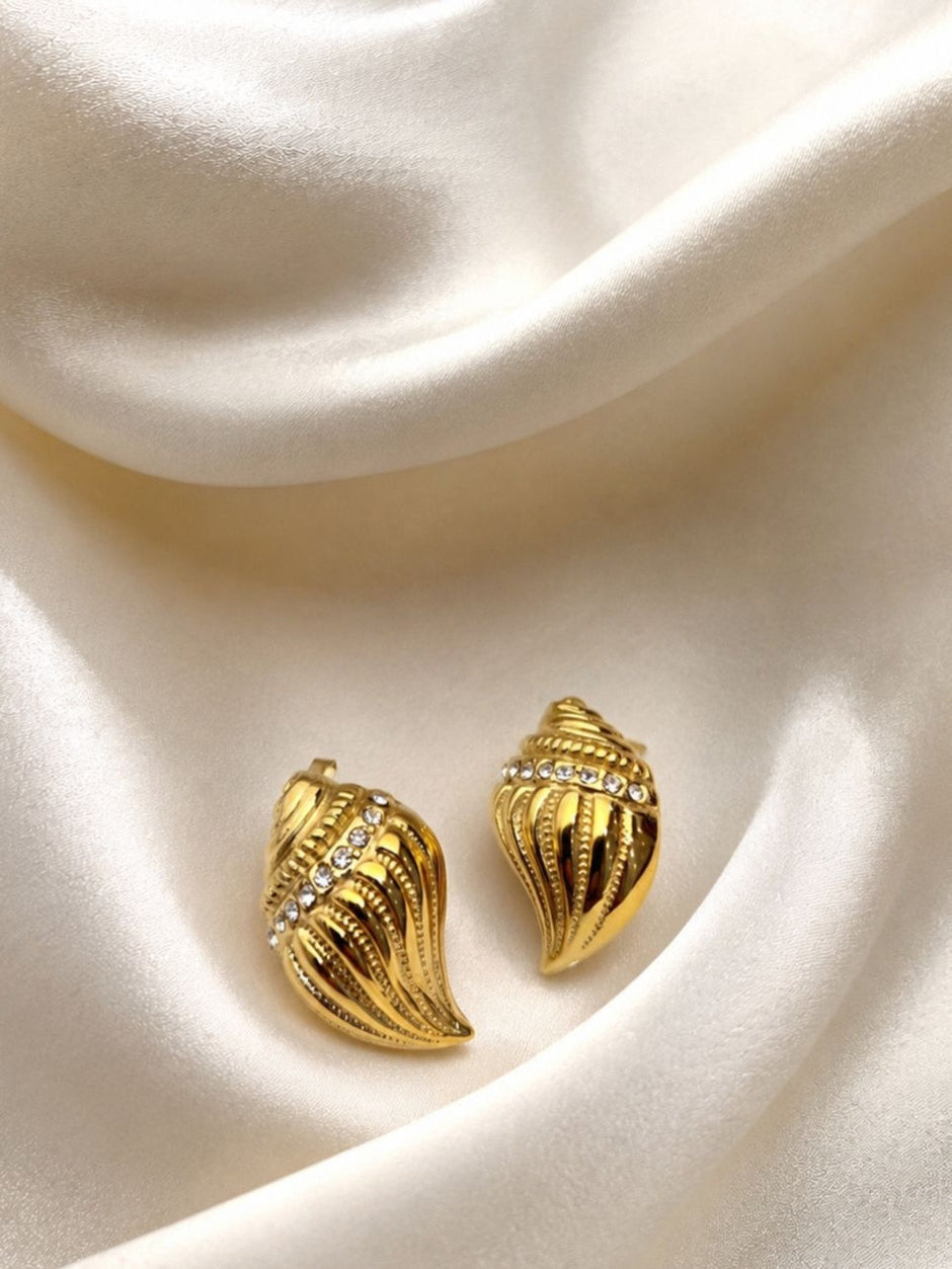 Pair of gold-toned conch shell stud earrings with crystal row on cream satin fabric