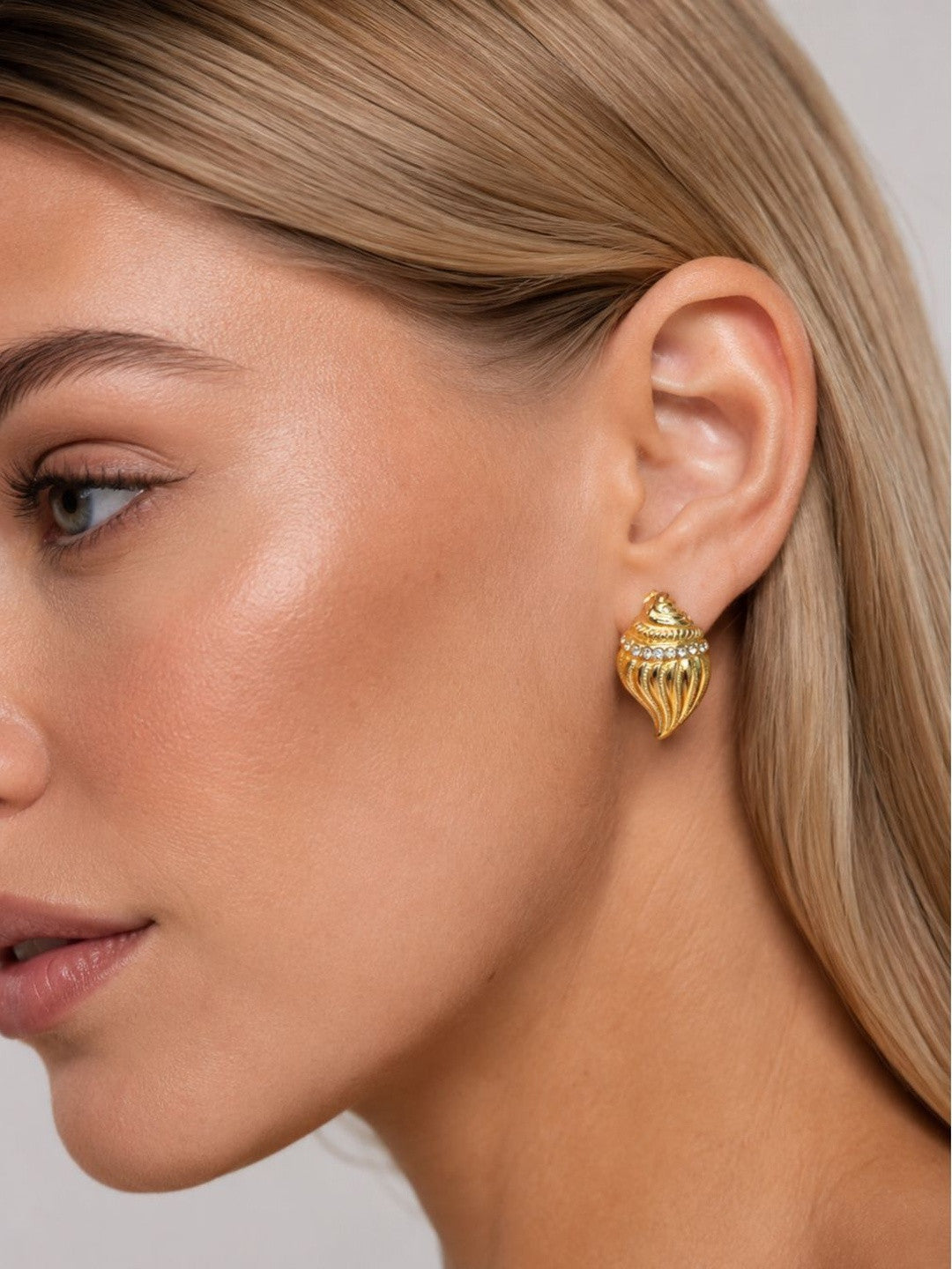 Woman wearing gold conch shell crystal stud earring on right ear, side profile view
