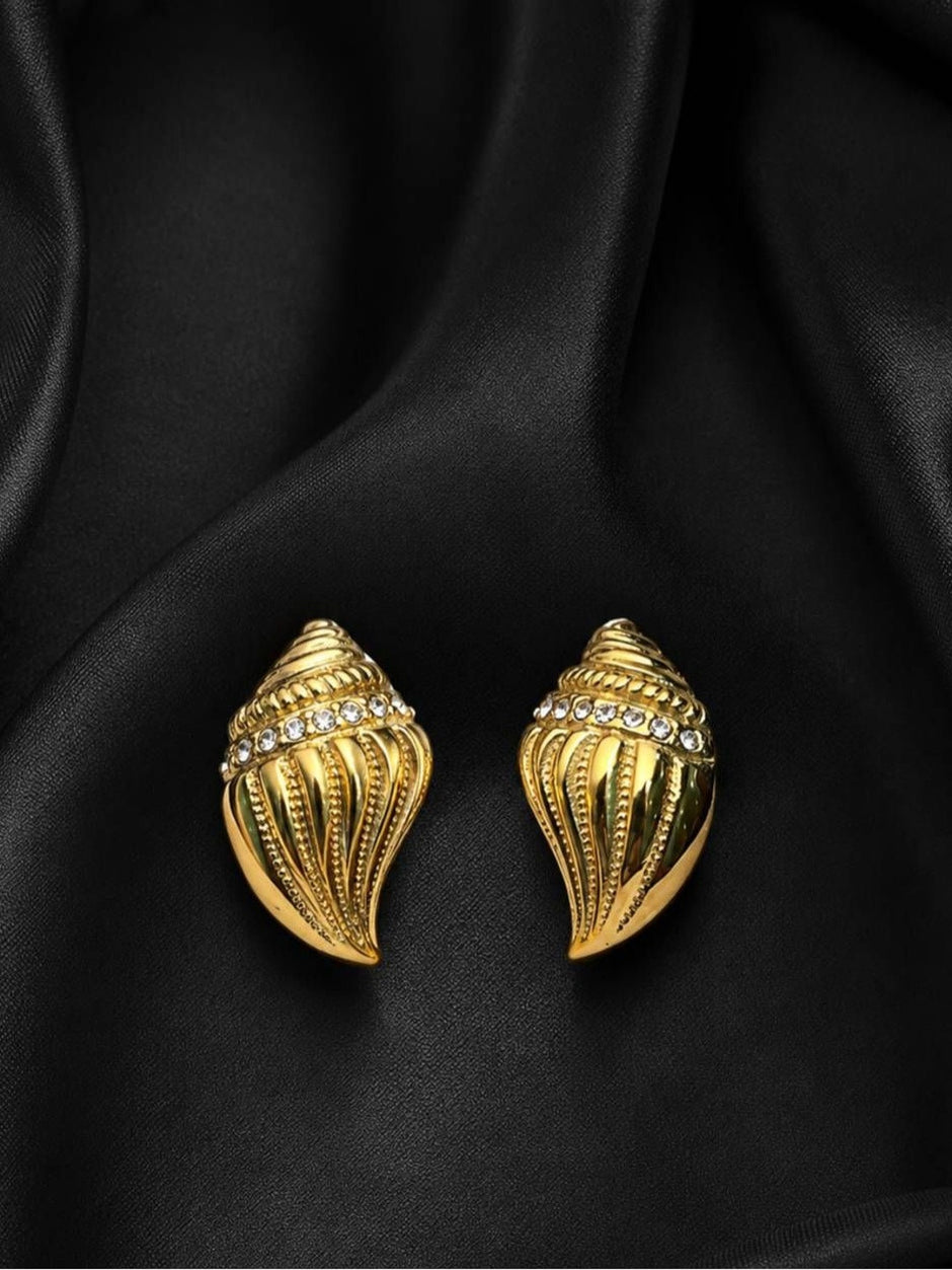 Two gold conch shell stud earrings with crystal band displayed on black satin fabric