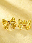 Front and back view of gold bow stud earrings showing push-back fastening on cream surface