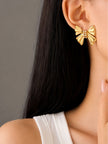 Gold bow stud earring worn on a woman's ear with dark hair and white top