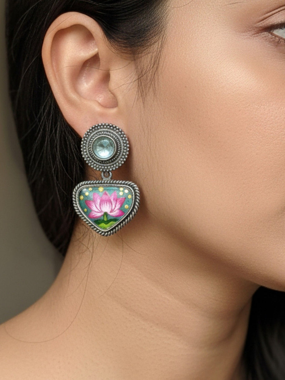 Woman wearing oxidised silver minakari lotus drop earring with light-blue stone stud top against neutral background