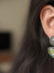 Close-up of oxidised silver meenakari stud earring worn on a woman's ear showing kundan top and green enamel drop