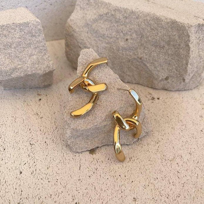 Gold plated abstract hoop earrings displayed on stone background, highlighting their bold, artistic and modern design.