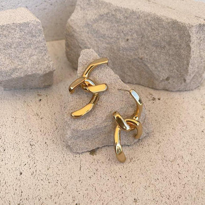 Gold plated abstract hoop earrings displayed on stone background, highlighting their bold, artistic and modern design.