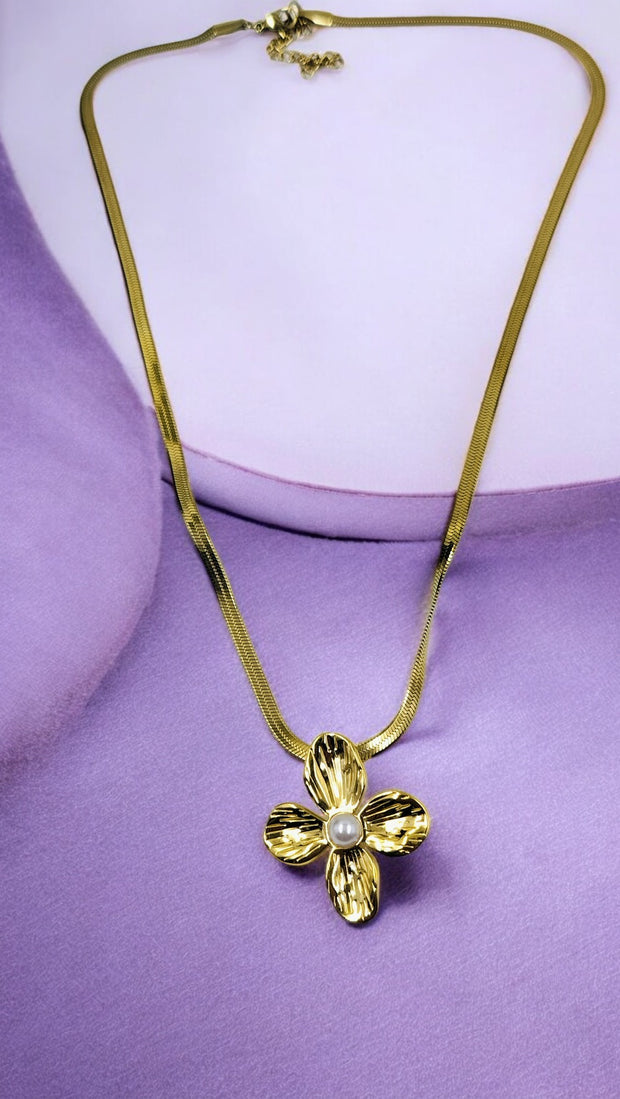 A gold floral pendant necklace with a pearl center on a snake chain laid out on a purple surface.