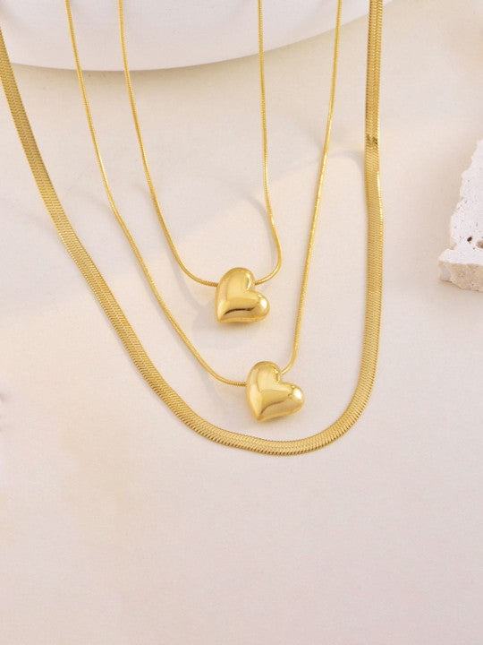 A set of gold-colored heart-themed chain necklaces with multiple layers, displayed on a stand, showing the necklaces in their layered arrangement.