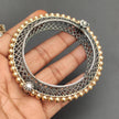Silver and gold bracelet held in a hand against a gray background