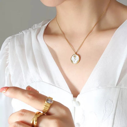 Gold necklace with round pendant featuring key design, worn with white outfit.