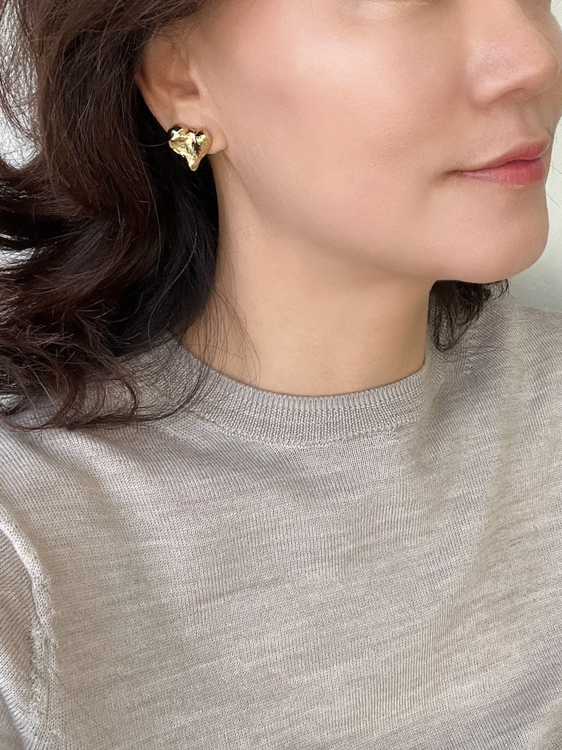 Gold plated abstract heart stud earrings worn by woman, elegant statement jewellery perfect for everyday wear and special occasions