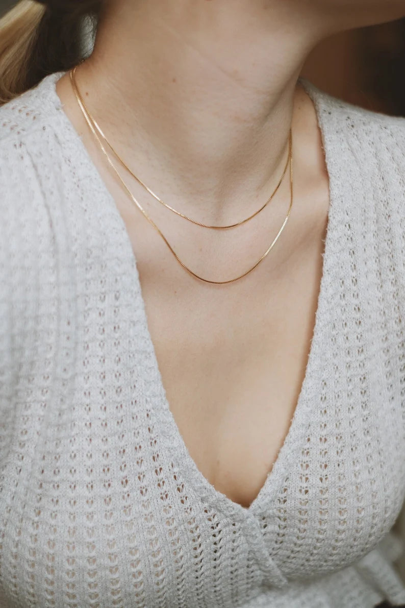 A person wearing a white knit top and gold double-layered chain necklace.