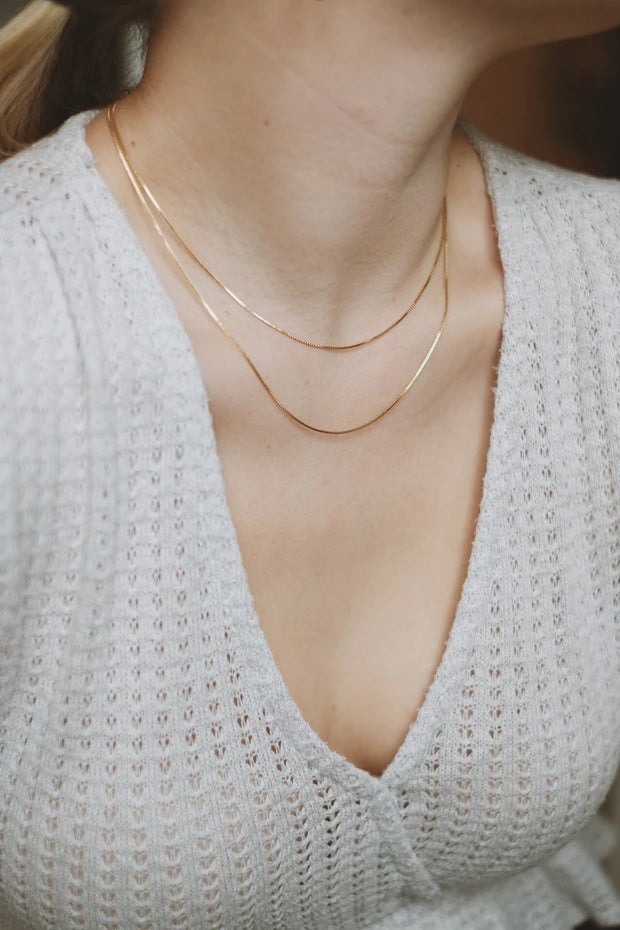 A person wearing a white knit top and gold double-layered chain necklace.