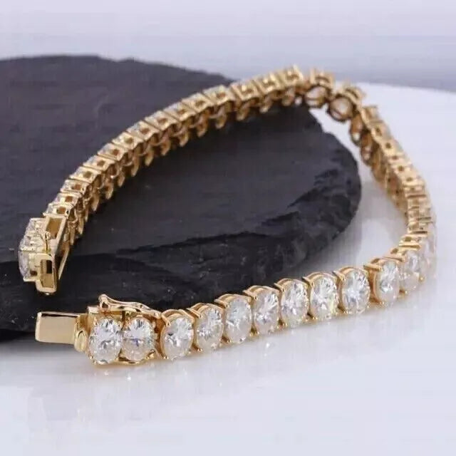 Gold tennis bracelet with large round-cut white stones placed on a black stone surface.