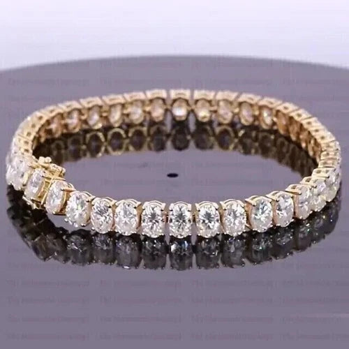 Elegant gold tennis bracelet featuring oval-cut white stones arranged in a continuous row, displayed on a reflective surface.