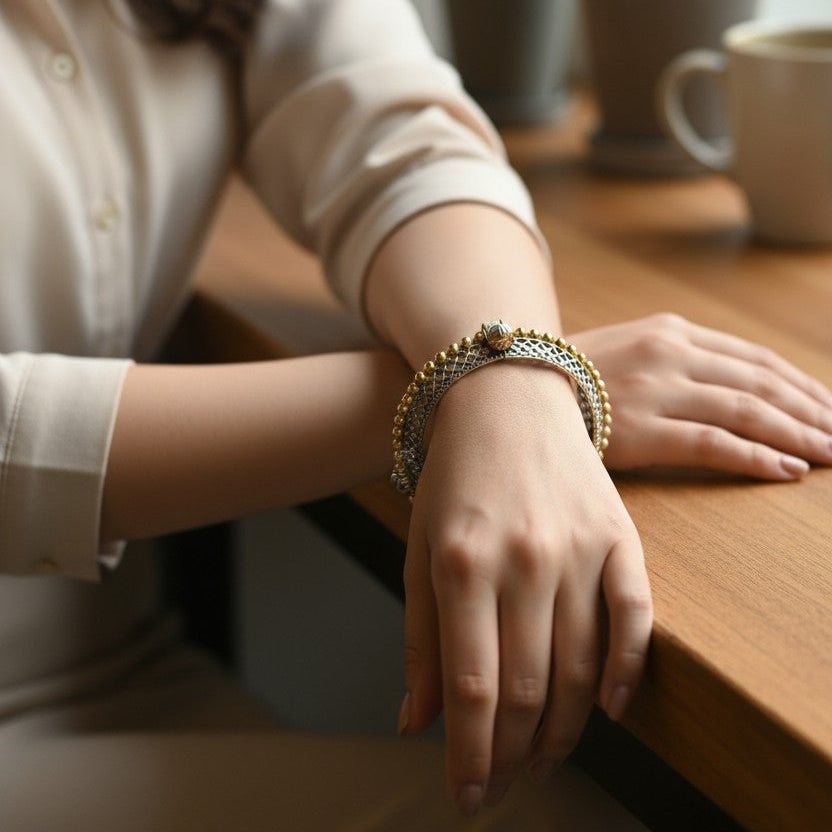 Person wearing a bracelet on a wooden table with plants in the background